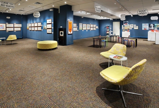 Blue Walls hung with Snoopy Cartoons in background, yellow modern chairs in foreground, activity tables and display cases